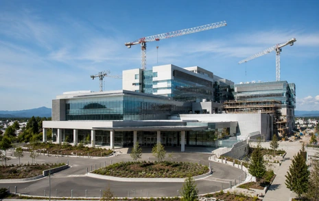 A modern hospital building under construction with cranes above it in Surrey BC