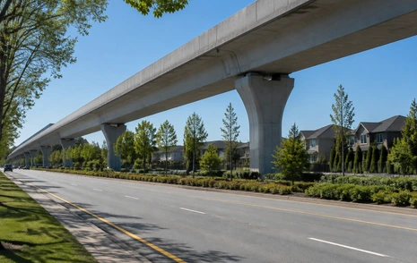 An elevated SkyTrain guideway under construction over a wide Surrey arterial road