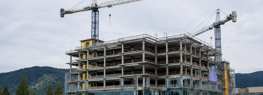 A modern hospital building under construction with cranes above it in Surrey BC