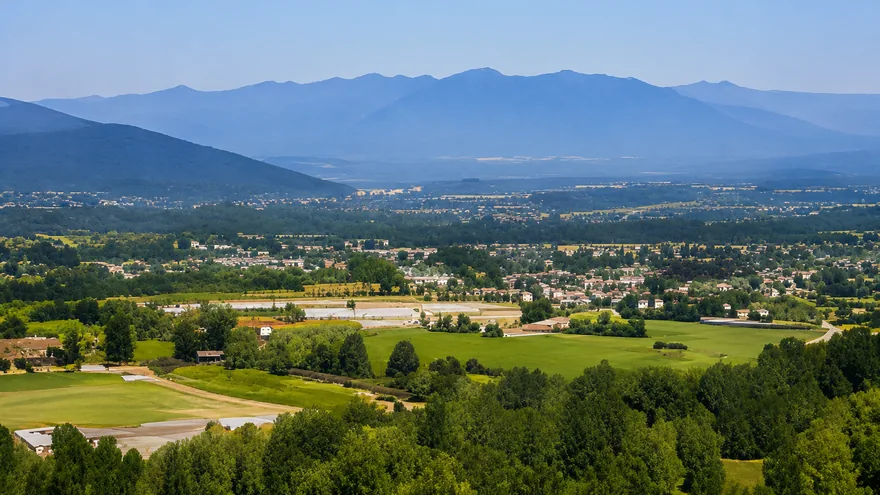 A wide Fraser Valley view of farm fields and a low town below hazy blue mountains, homes for sale in Abbotsford BC