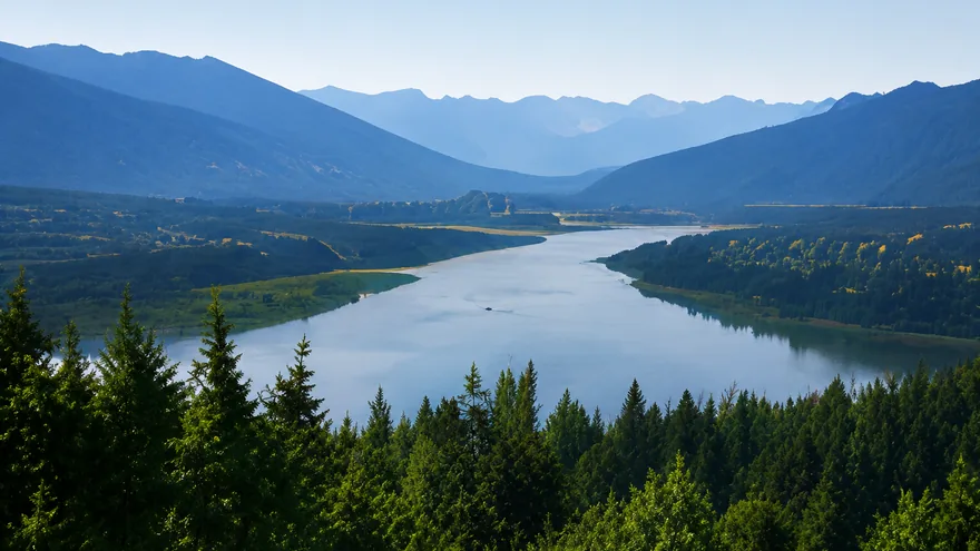 The Fraser River curving between forested hillsides below layered blue mountains, homes for sale in Mission BC