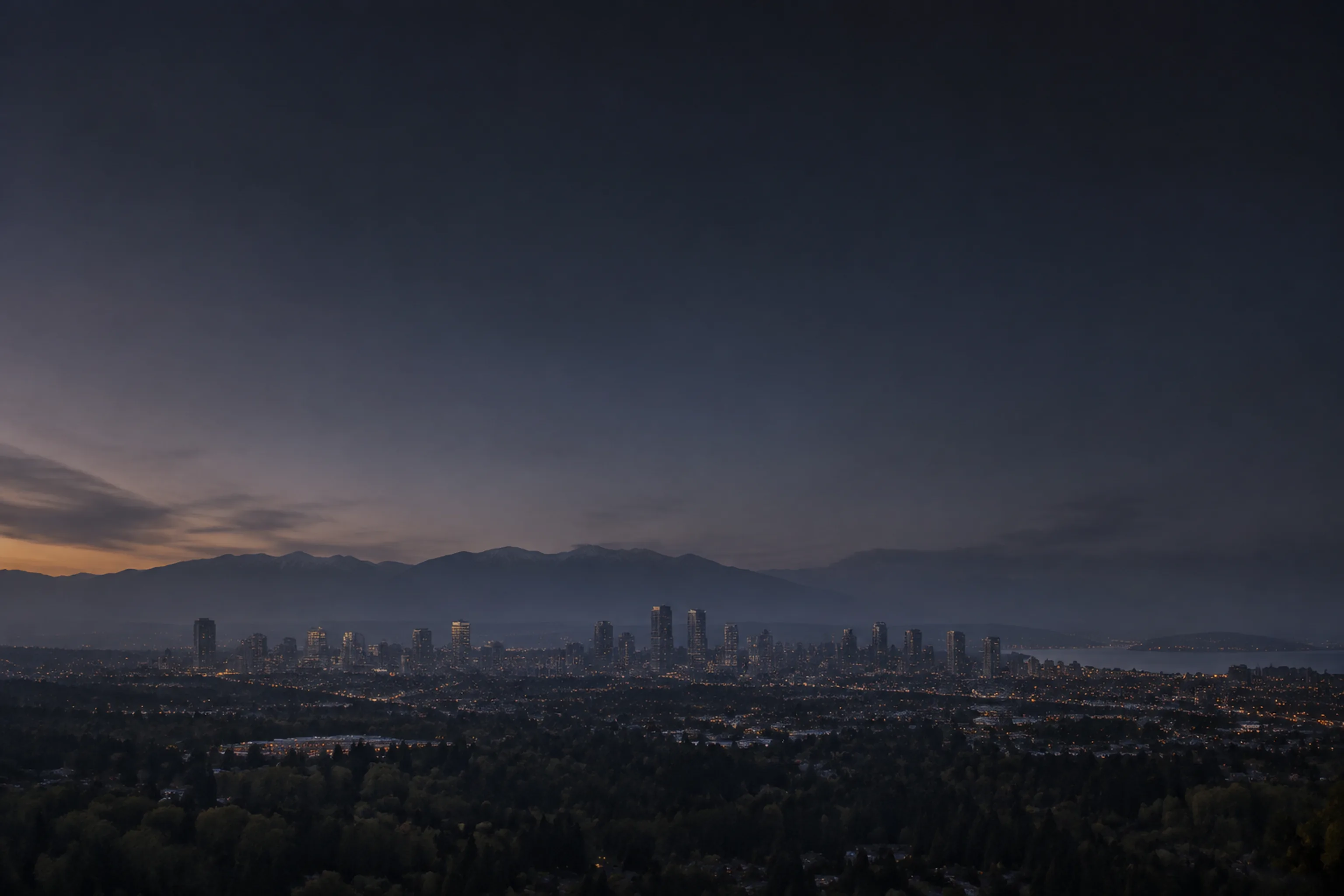 A hazy dusk view across a distant Lower Mainland city skyline with the North Shore mountains on the horizon