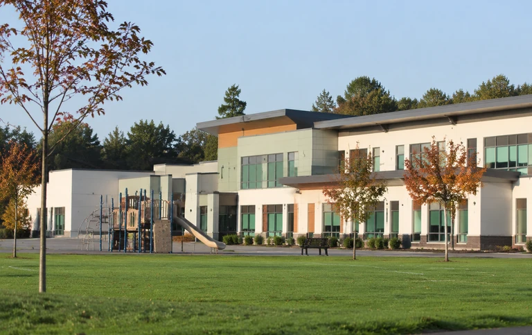 A modern low rise suburban elementary school seen across a wide green playing field with young maples on a bright morning