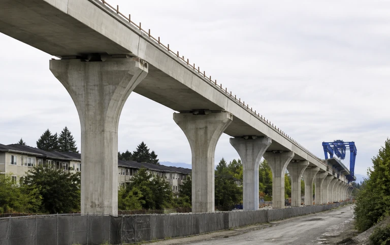 A long line of completed elevated guideway piers marching into the distance along a suburban corridor, with the deck placed on most of them